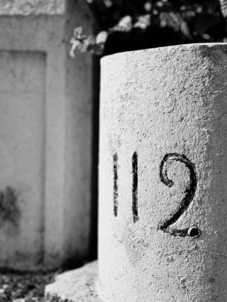 Close-up of a mile marker with the number '112' written on it.