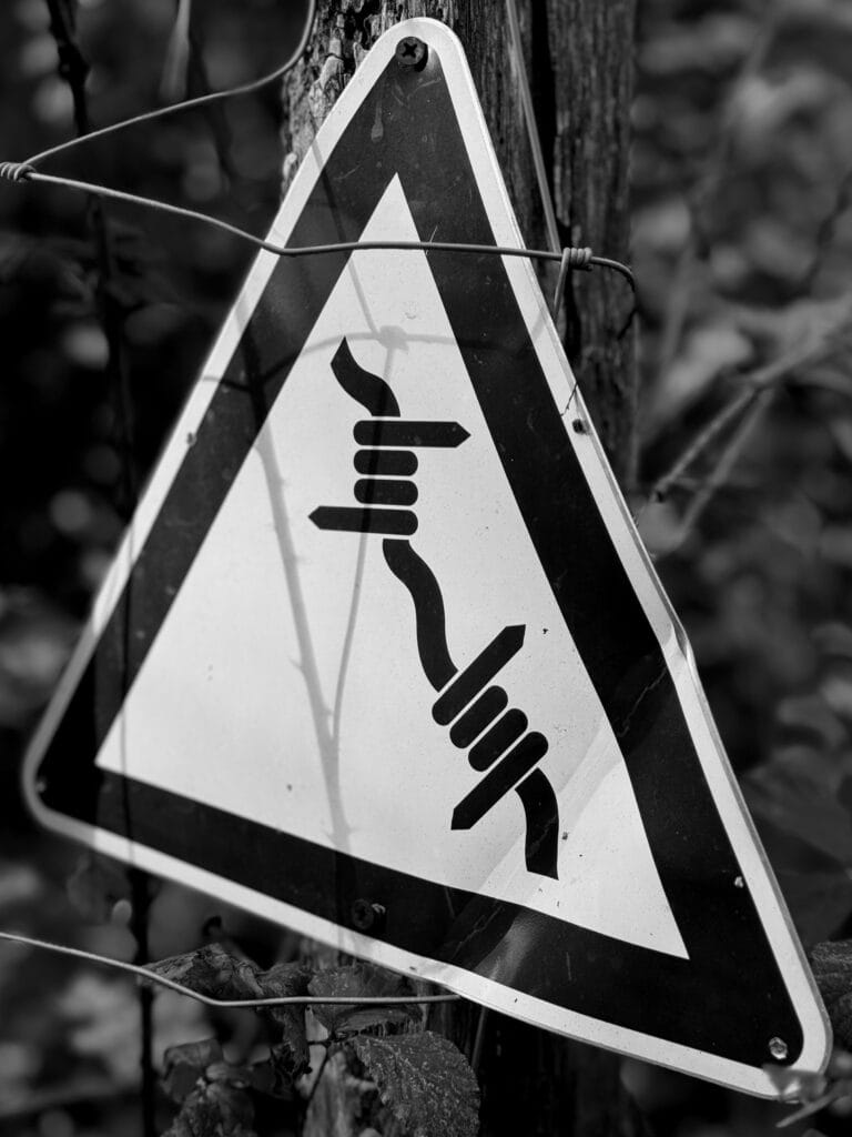 View of a ‘caution barbed wire’ sign on a fence post.
