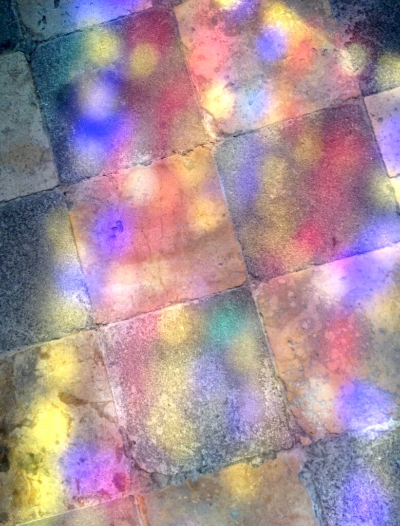 Small paving stones on the floor, lit by light through a multicoloured stained-glass window.