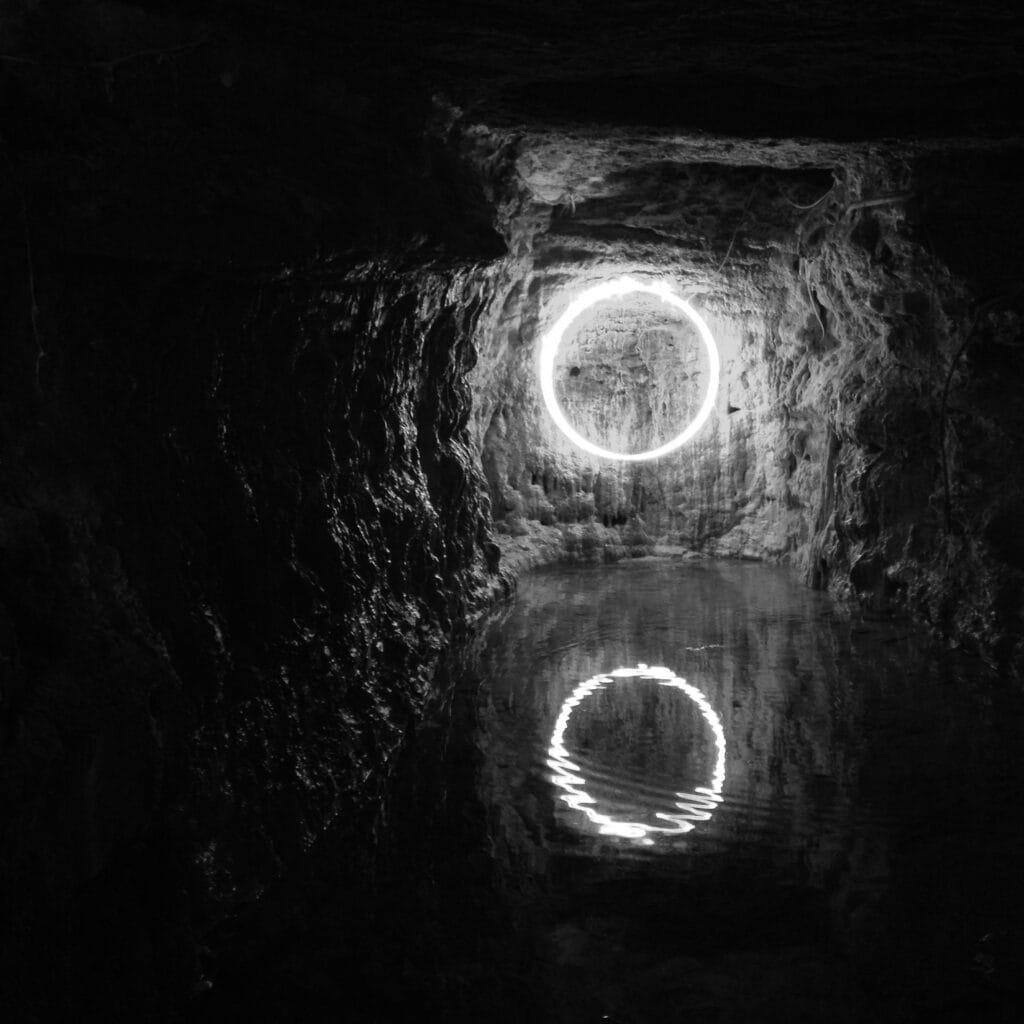 View of a small cave at night, with its lake reflecting a circle-like neon light fixed to the back wall.