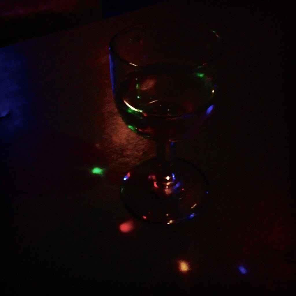 A small, round glass with a stem reflects the light from a multicoloured garland, creating small, coloured dots all around.