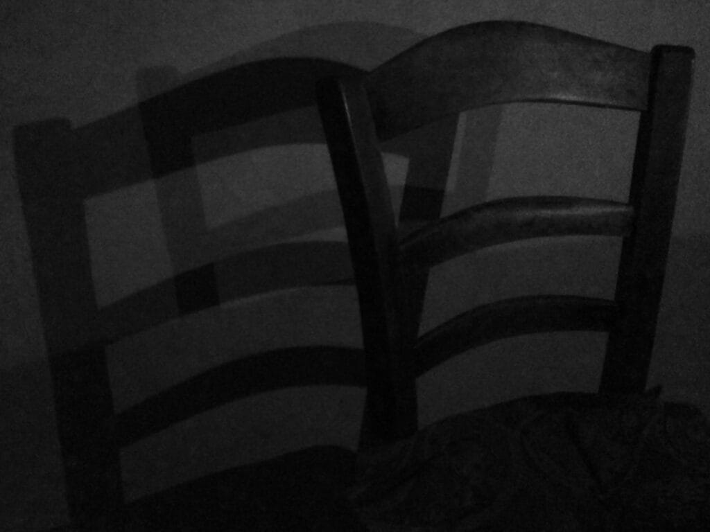 A candlelit chair sits back from the wall, casting a dark shadow on the left and a light shadow on the right.