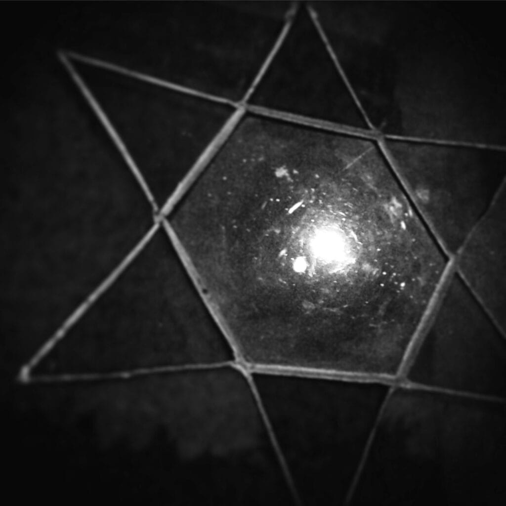 A close-up of a star-shaped stained glass through which the full moon is visible.