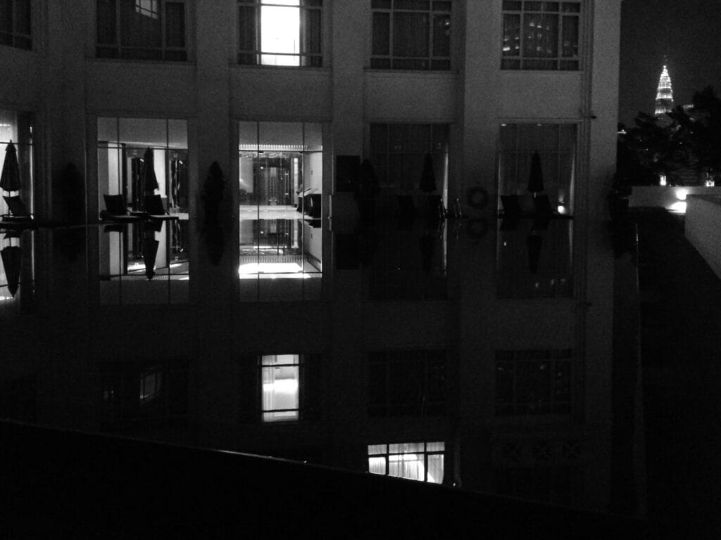Petronas Towers at night, viewed from a swimming pool on a terrace.