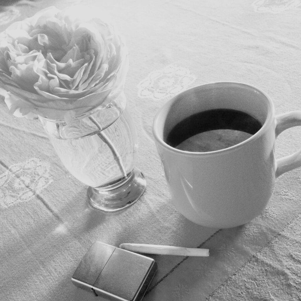 A morning still life featuring a cup of coffee, a cigarette, a lighter and a rose on a table.