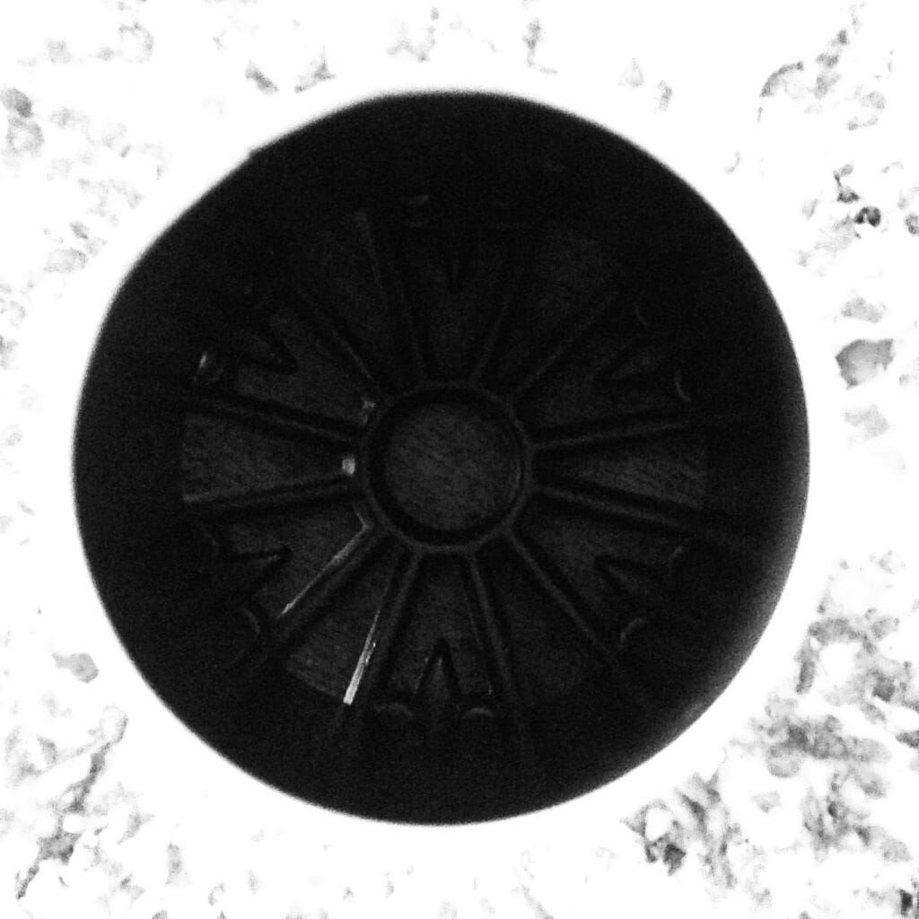 A close-up of the centre of a cake baked in a savarin mould and placed on a cast-iron trivet. The cake forms an overexposed halo around the shadowed centre of the trivet.