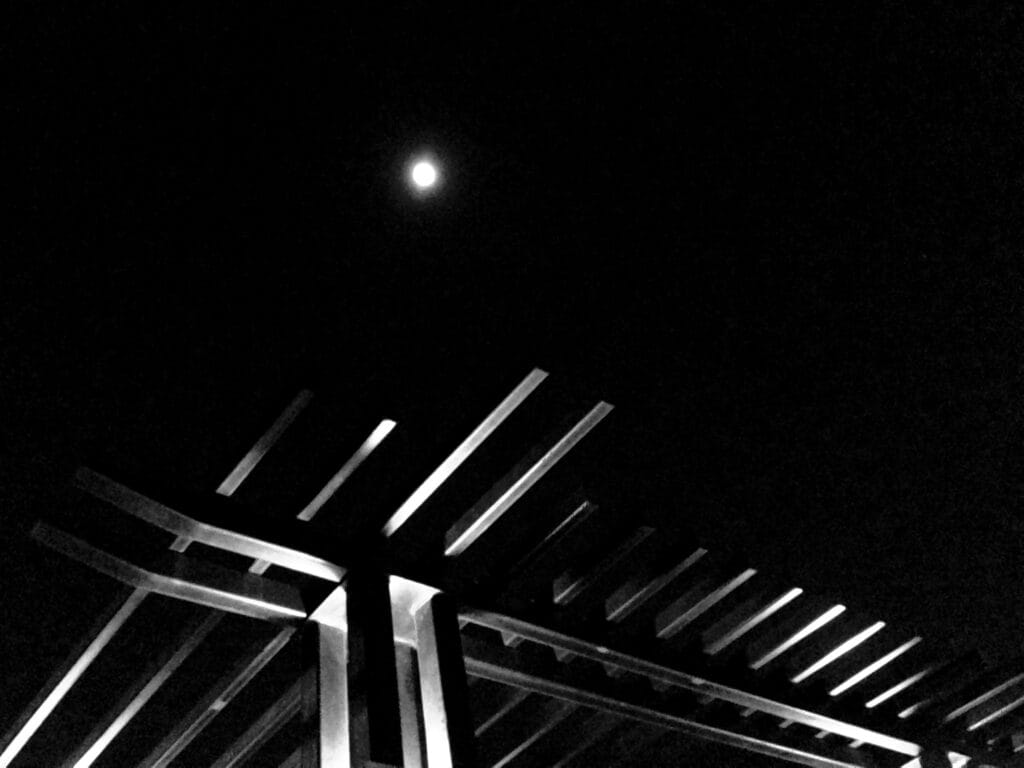 Low-angle view of a torii-alike structure against a night sky with a full moon.