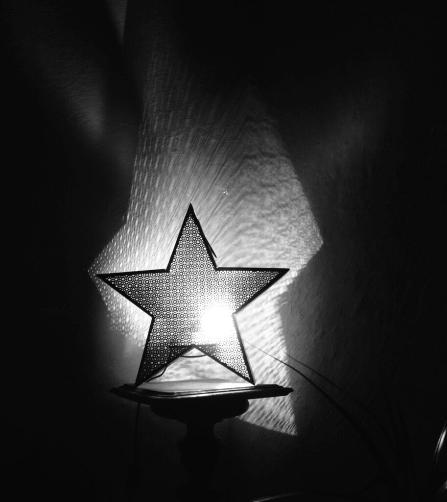 A star-shaped black metal lamp casts geometric shadows onto the walls of a dark room.