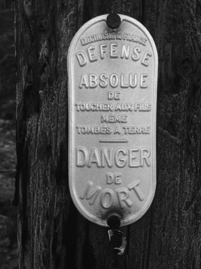 Vintage French energy supplier sign on an electric post which reads: 'Do not touch the wires, even if they have fallen to the ground. DANGER OF DEATH.'