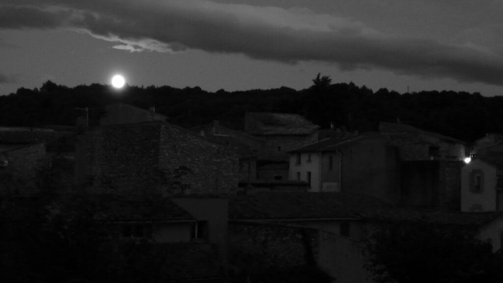Vue nocturne dal village adossæ al colline, de derrière læquæl læ plæn lune monte sur læ côté gauche de l’image.