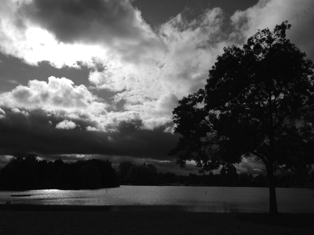A view of an island from the shores of a lake, backlit by the setting sun hidden behind clouds.