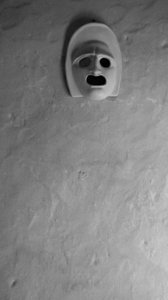 Earthen mask on a wall, with the tormented expression of someone screaming.