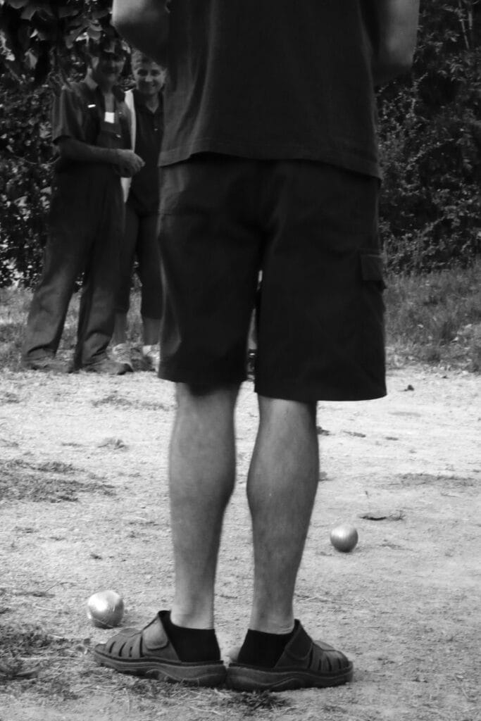 One player stands with er feet behind the jack on the pétanque strip, indicating the target to his teammates.