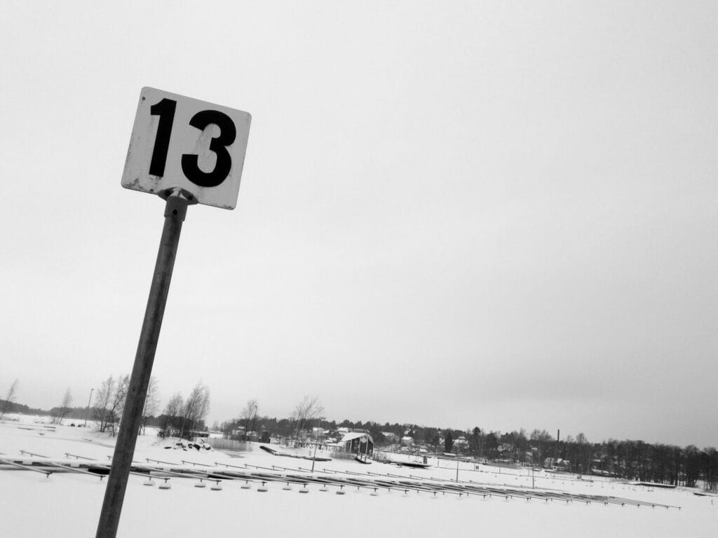 View of the deserted shores of a lake under a snowy sky. In the foreground a sign with the number 13.
