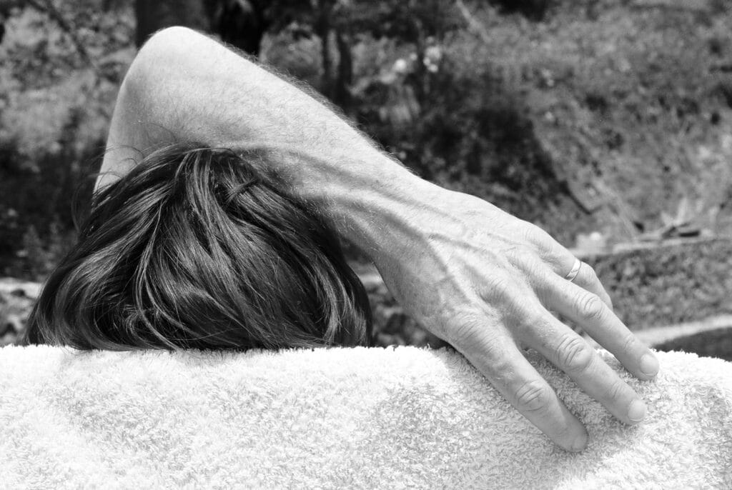 From behind, the head of someone napping on a deck chair with an arm over it to protect er eyes.