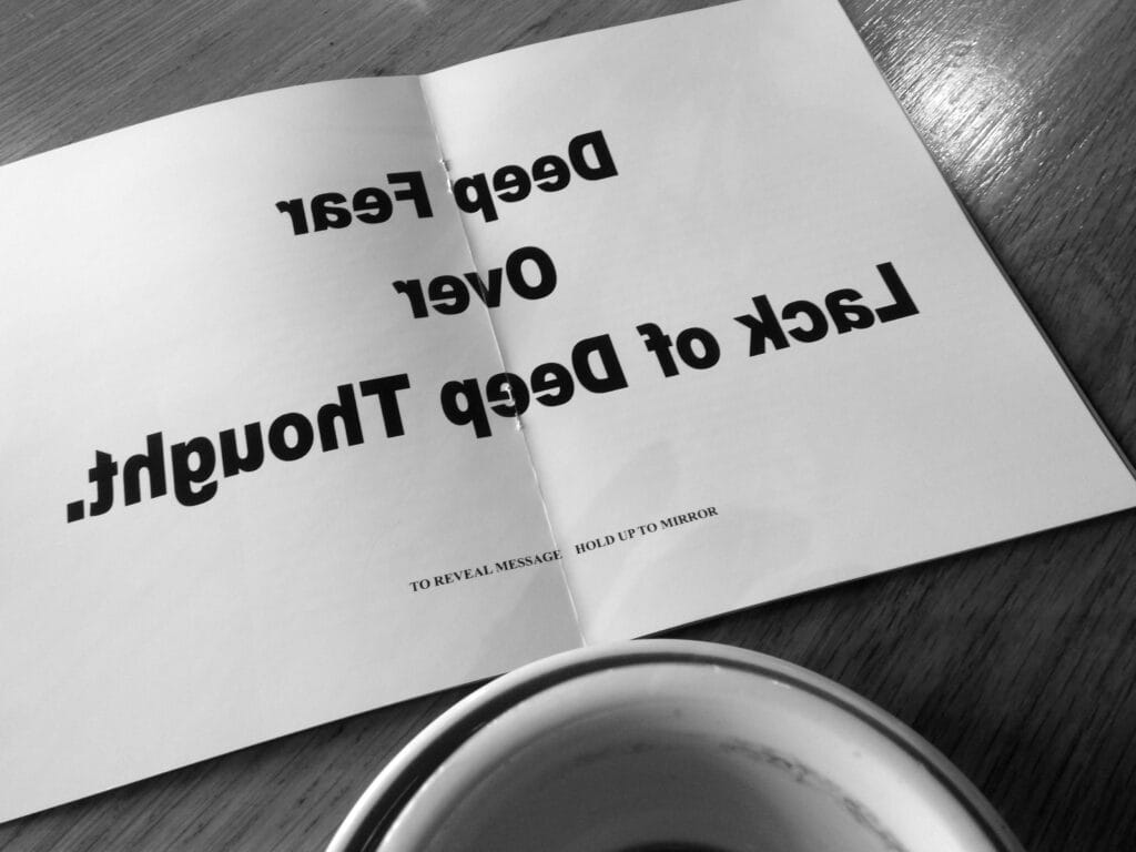 Placed on a café table, a fanzine has the following text written in mirror: ‘Deep Fear Over Lack of Deep Thought. (To reveal message, hold up to mirror)’.