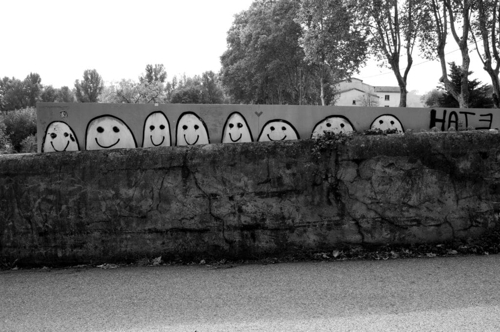 Bunch of little people and the word 'hate' graffitied behind a long sign above a low wall.