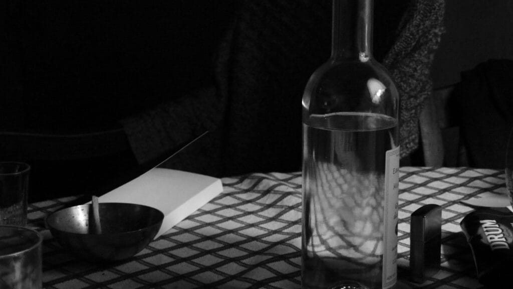 Still life with a packet of tobacco, a Zippo, a bottle of brandy, an ashtray with a fag in it, a glass (for the brandy), a book on the checked tablecloth, Granpa's waistcoat on the armchair by the fire. All lit by candlelight.