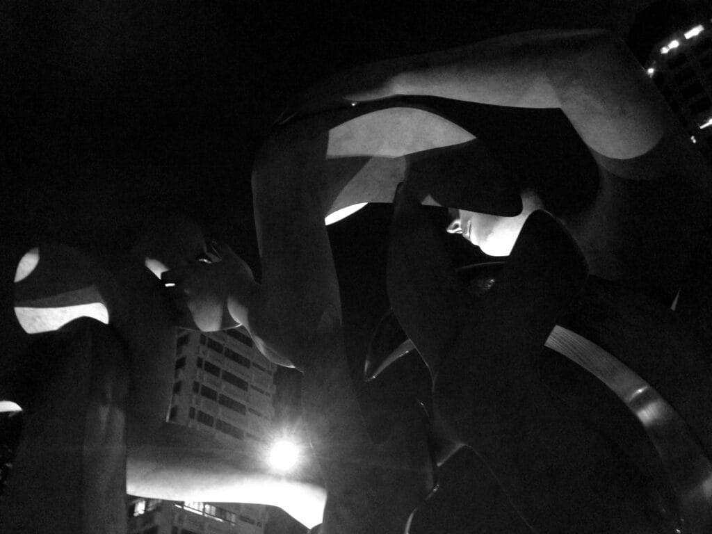 Stone statues and a backdrop of buildings at night.