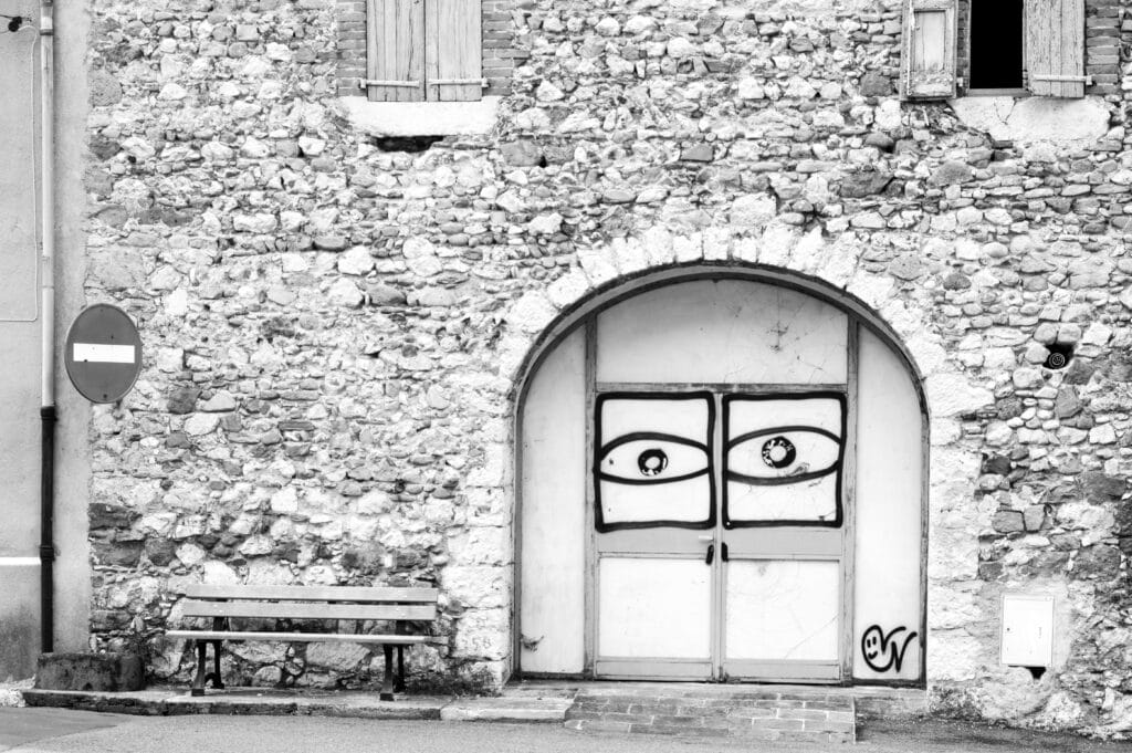 Façade d’æn maison sur læquæl est fixæ æn panneau 'sens interdix'. Sur les portes dal porche sont taggæs deux yeux qui surveillent læ rue.