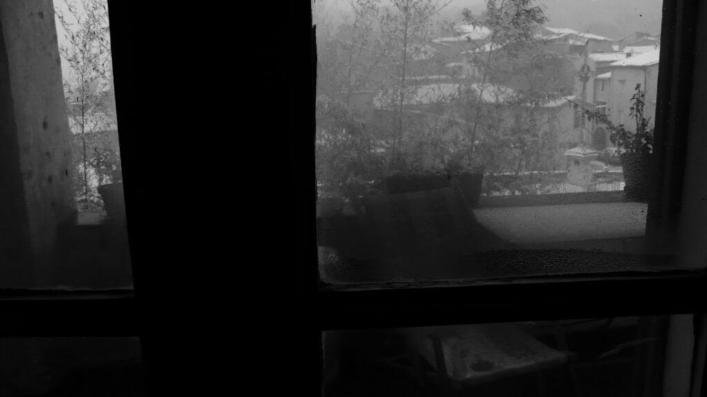Droplets of condensation on the inside of a window overlooking a snow-covered village.