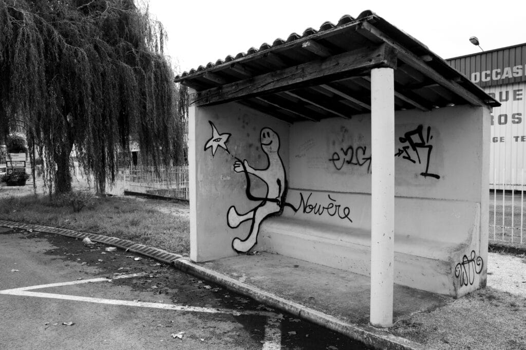 In a bus shelter, graffiti of a character as if e were sitting on a bench. E is holding a string that forms the word ‘nowhere’ at one end. At the other end is a star like a balloon, with an eye.
