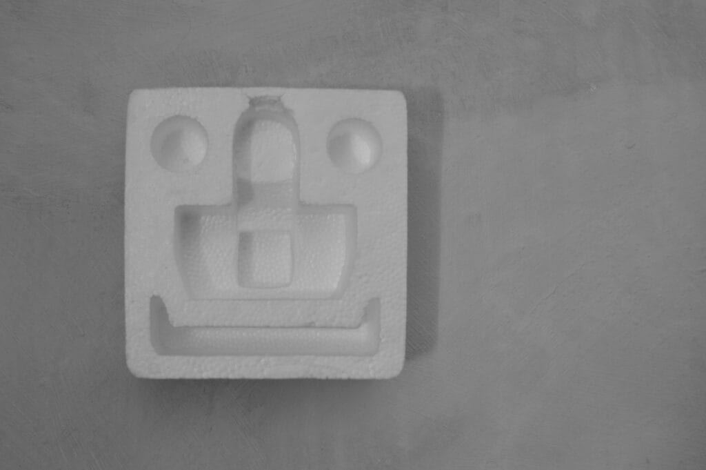 A polystyrene package cushioning section is displayed on a wall, with eyes, nose and smile holes.