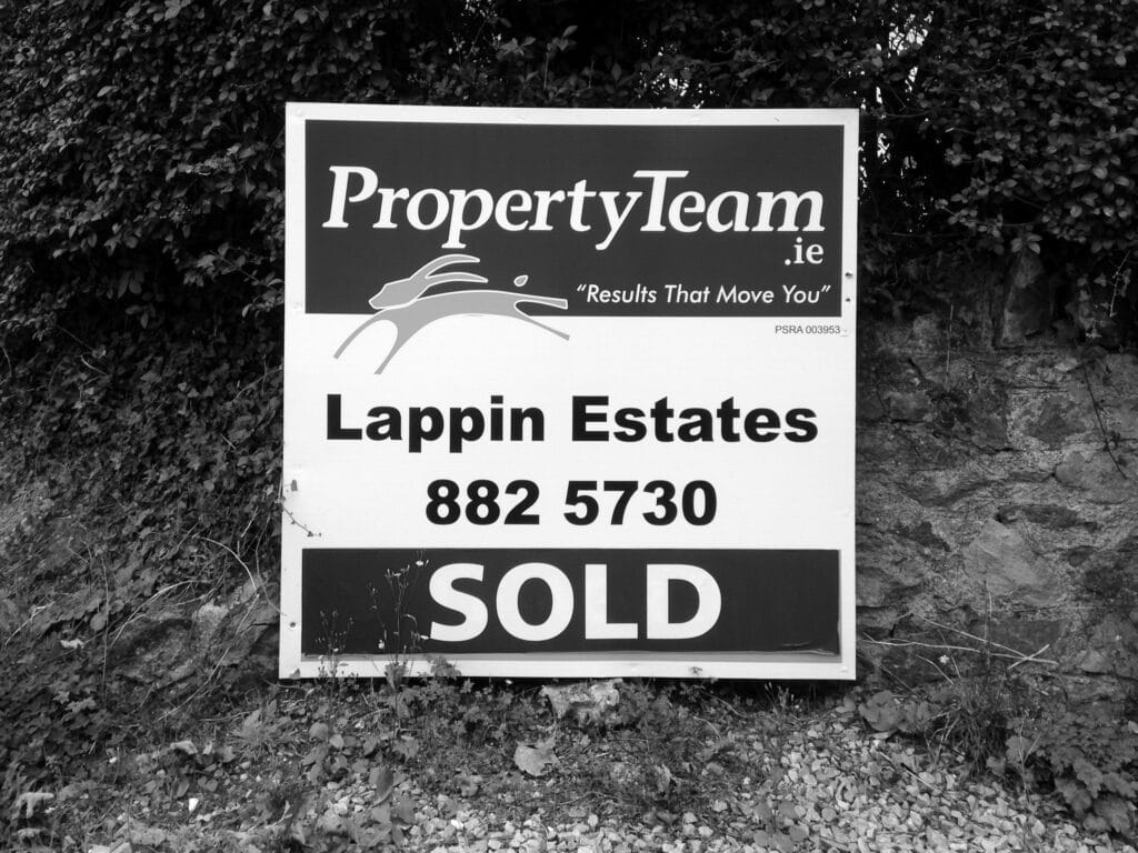Panneau devant æn maison sur læquæl on lit: 'PropertyTeam.ie, Results That Move You. Lappin Estates. SOLD'. En françæ: adresse d’æn site internet qu’on pourrait traduire par 'l’équipe dal immobiliær', avec l’extension de l’Irlande (.ie); slogan 'Des résultats qui vous font bouger' (?); domaine Lappin; VENDU.