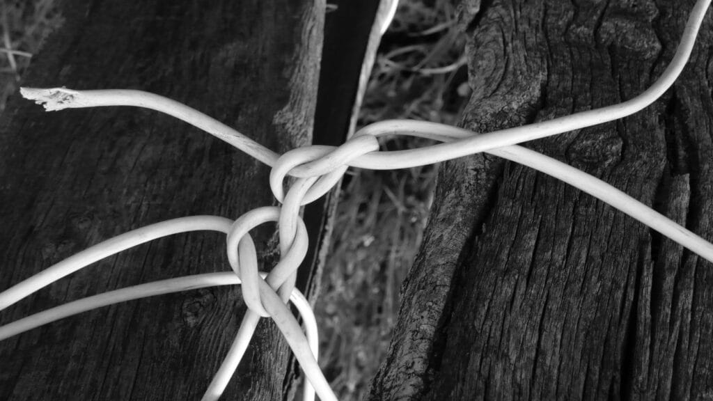 A tangle of electrical wires knots on a fence post.
