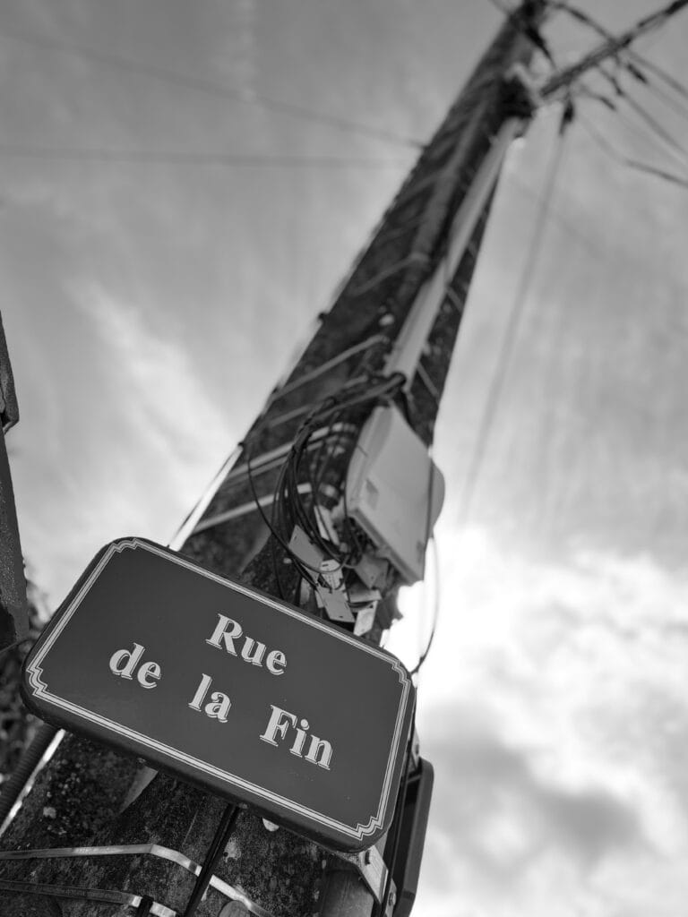 Street sign on a pole photographed from below against the sky, indicating ‘Rue de la fin’ (literally ‘End Street’).