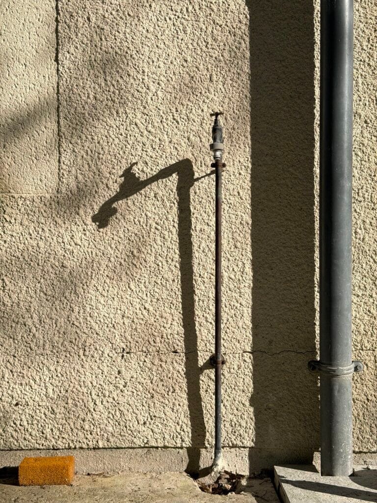 An outdoor tap and er shadow cast on the wall.