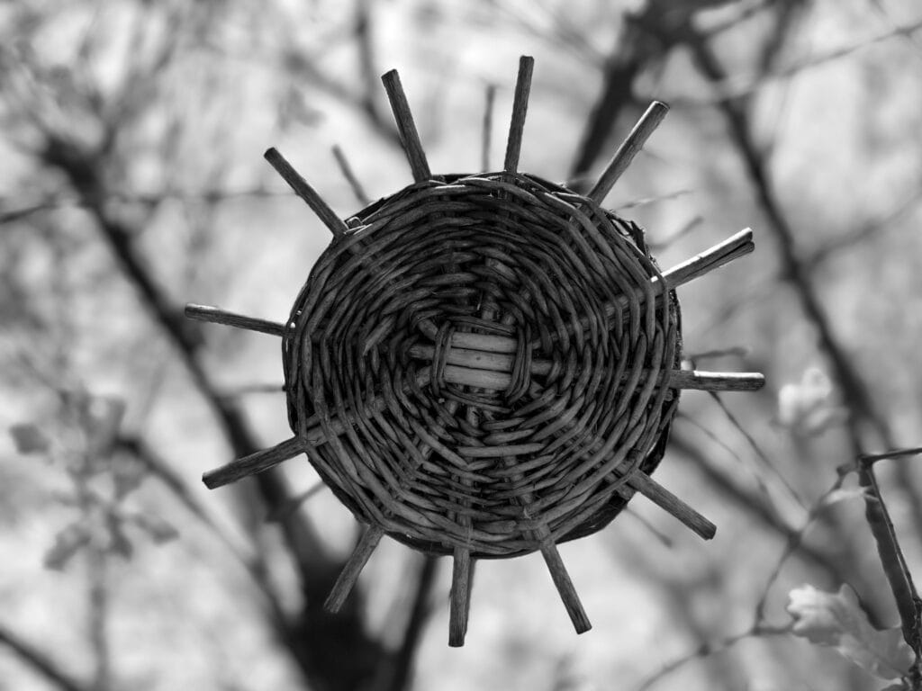 A round wicker bird feeder with protruding spokes, seen from below. It looks like a sun.