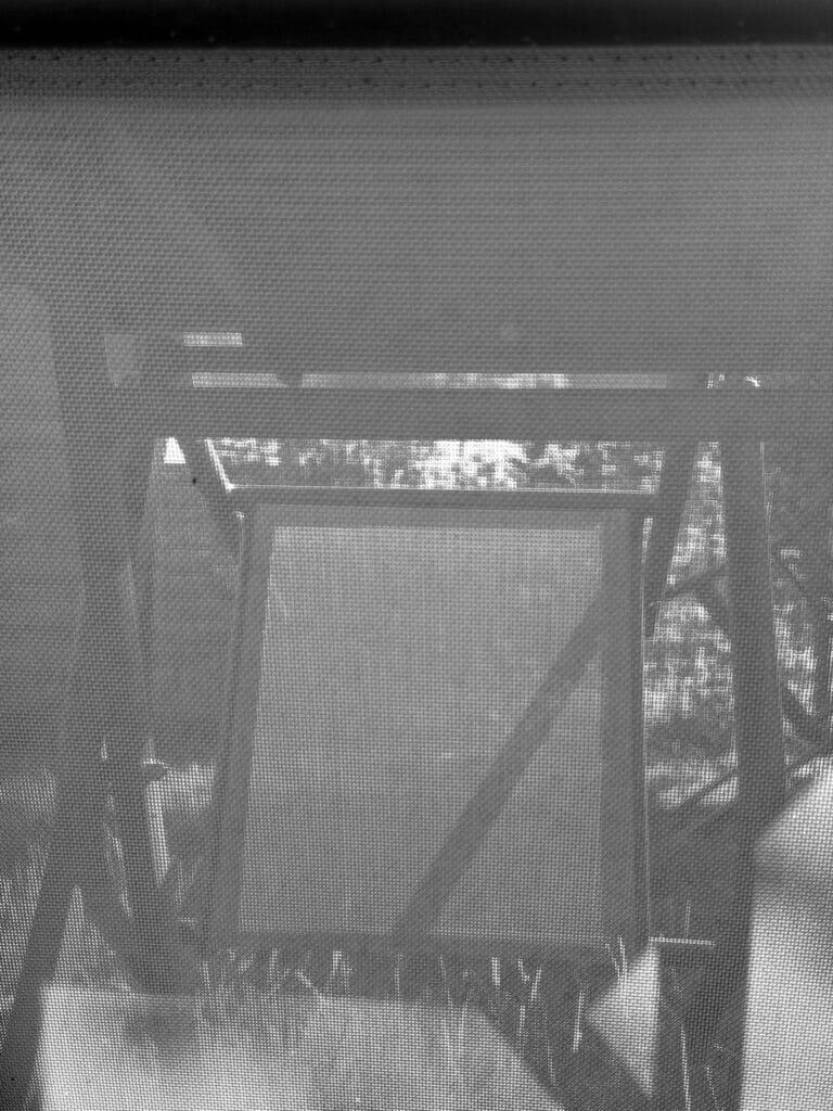 The underside of a garden table and the legs of the table and chairs, seen through the fabric of a garden chair.