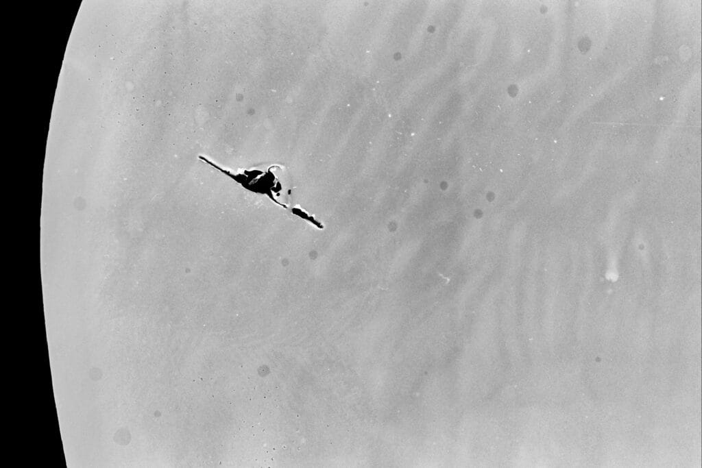 A scan of a piece of film showing a curved, mottled surface in shades of grey against a black background – it could be a fragment of the moon, with a notch from a film clip that might resemble a spaceship.