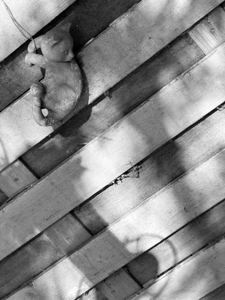 A ceramic cat hanging from a wire on a fence.