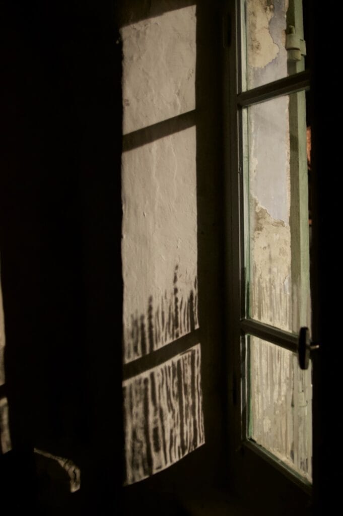 Light from a street lamp shining onto a wall through a window painted with vertical white stripes.