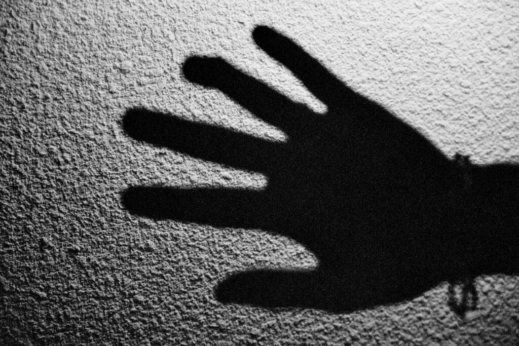 The shadow of a hand on a textured wall, with one finger bent.