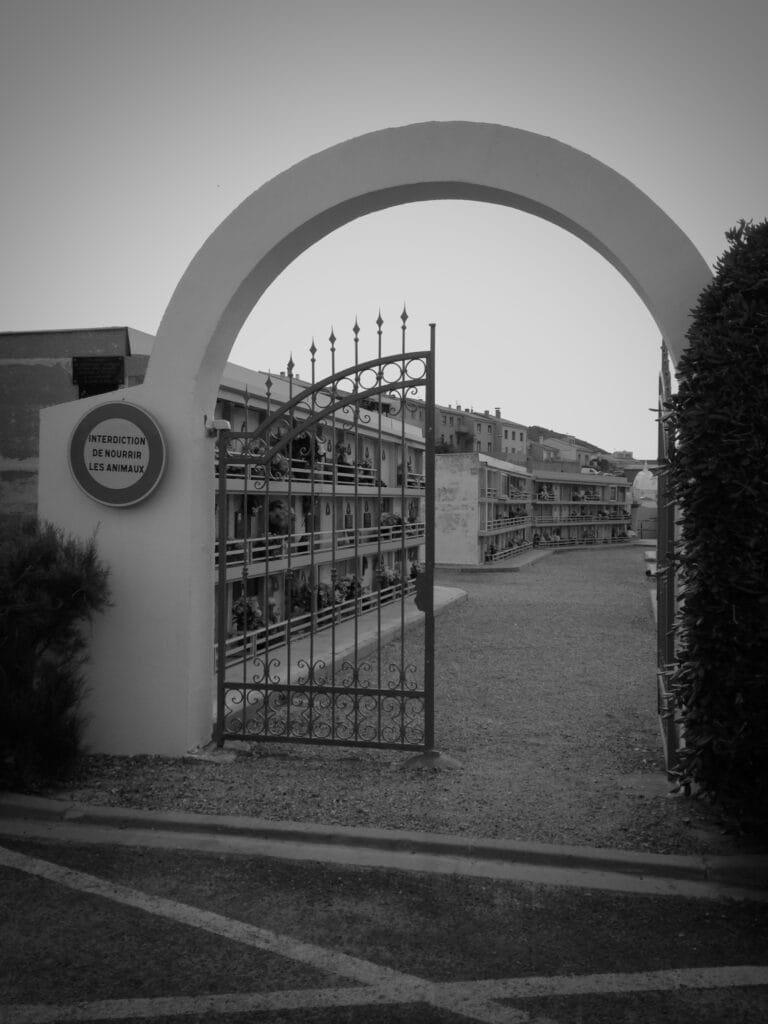 The entrance gate to a cemetery. On the wall is a sign reading ‘Interdiction de nourrir les animaux’ (‘Do not feed the animals’ in French).