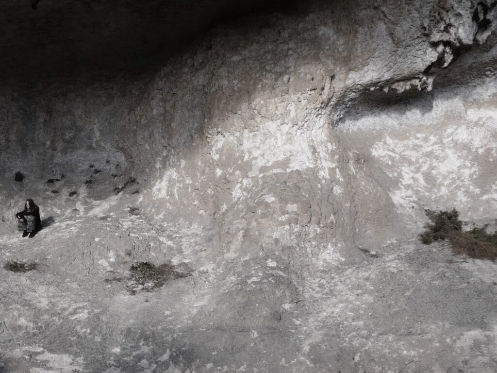 A person sitting on a rock beneath a cliff overhang.