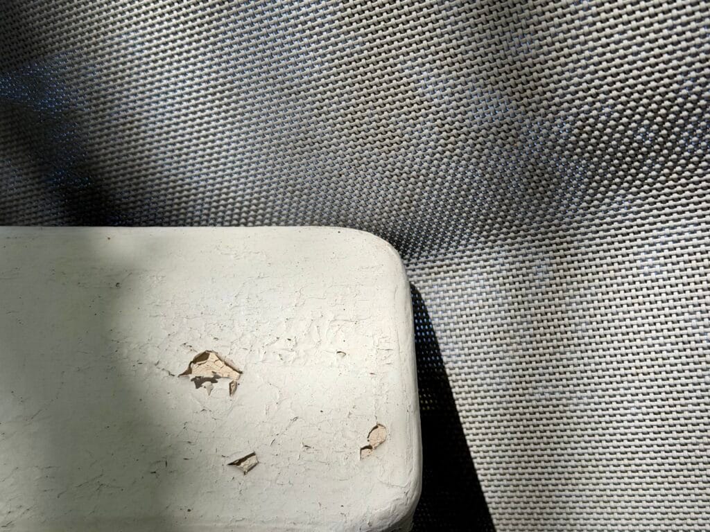 The fabric of a garden armchair leaning against the back of a bench with peeling paint. The weight causes the fabric to sag slightly.