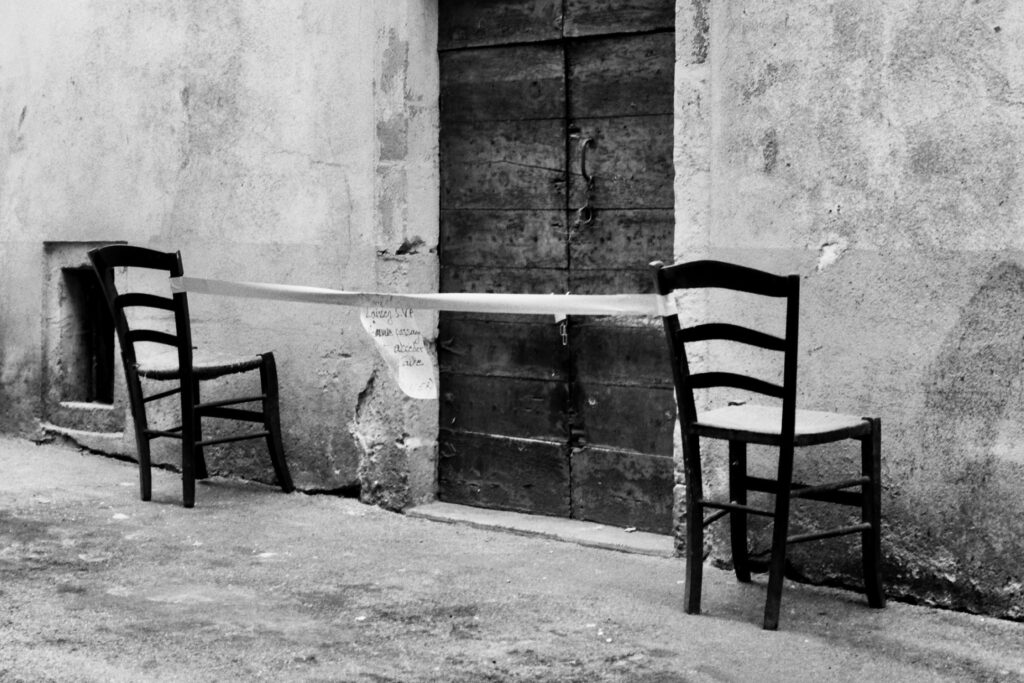 A ribbon stretched between two turned chairs in front of an old door in a narrow alleyway. A note attached to the ribbon reads: ‘Please leave a clear path to the cellar’.