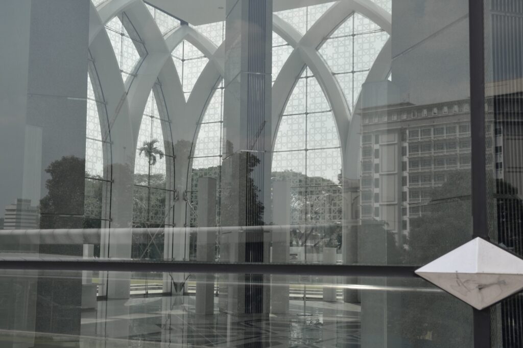 View of a building lobby through a large window, revealing the pointed-arch structure and the reflection of surrounding buildings.
