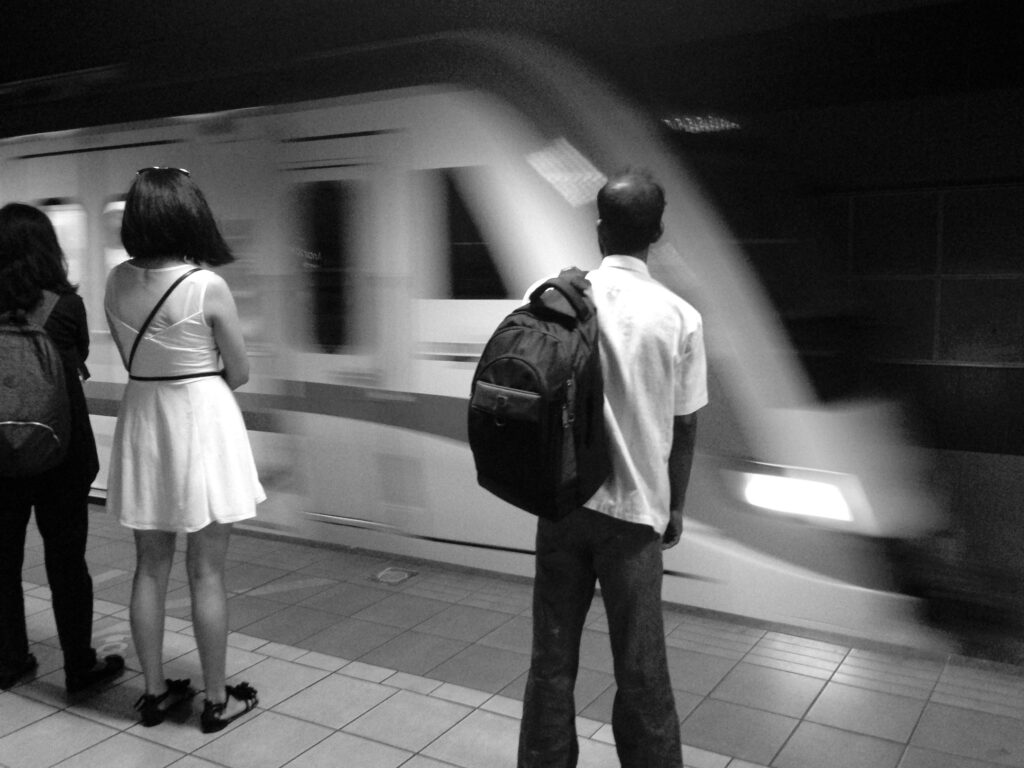 A subway train arrives at an underground station. Three people, seen from behind, are waiting on the platform.